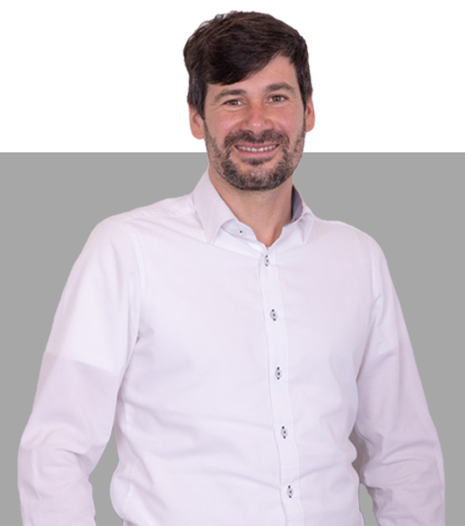 Herr mit braunen Haaren trägt ein Hemd und lacht in die Kamera.